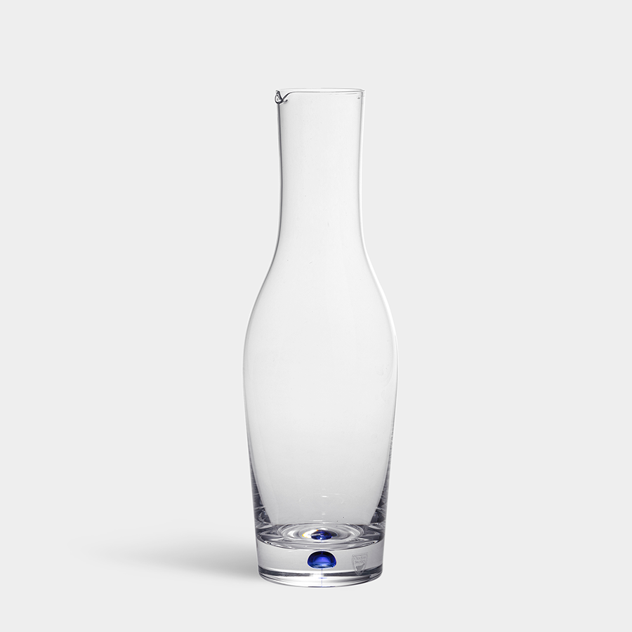 The Orrefors: Intermezzo Blue Carafe 37oz, by Erika Lagerbielke, showcases a clear glass design with a slender shape and subtle blue accent at the base, elegantly positioned against a plain white background.