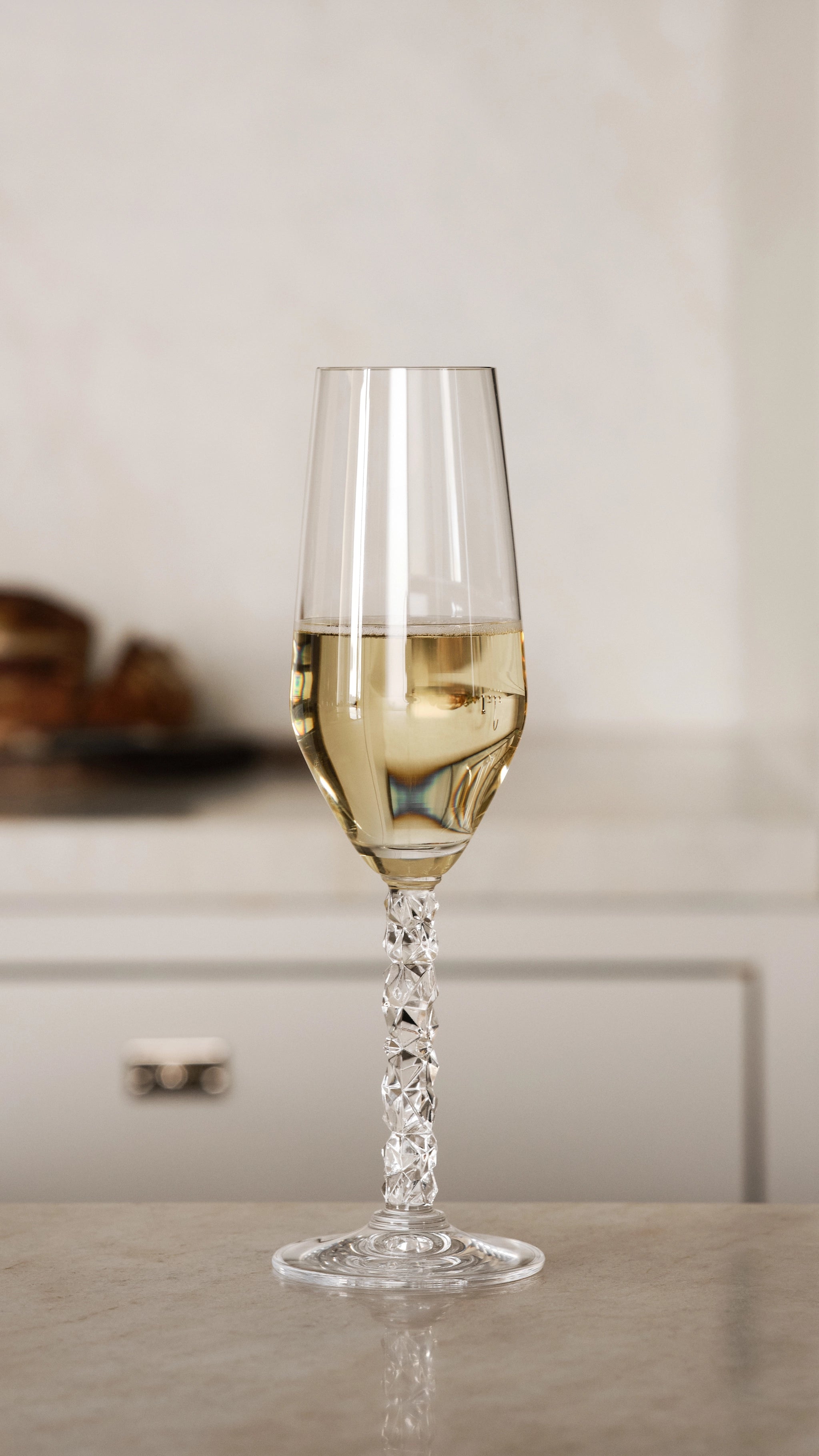 An Orrefors Carat Champagne Flute from the 8oz 2-Pack, half-filled with white wine, sits elegantly on a marble countertop.