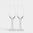 Two elegant Orrefors Carat Champagne Flutes, each 8oz with decorative stems, sit gracefully against a plain white backdrop, epitomizing the sophistication of the Carat Collection.