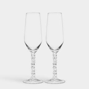 Two elegant Orrefors Carat Champagne Flutes, each 8oz with decorative stems, sit gracefully against a plain white backdrop, epitomizing the sophistication of the Carat Collection.