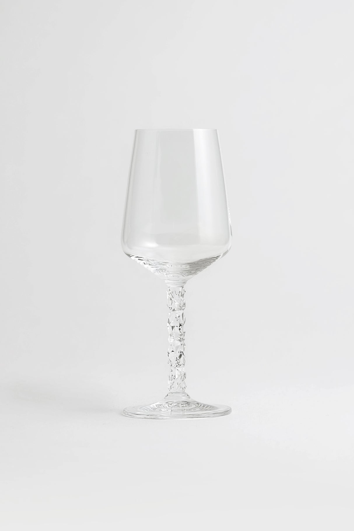 A pair of Orrefors Carat Wine Glasses (14.8oz) with textured stems stand elegantly on a white surface, highlighting their crystal clarity against a plain light background.