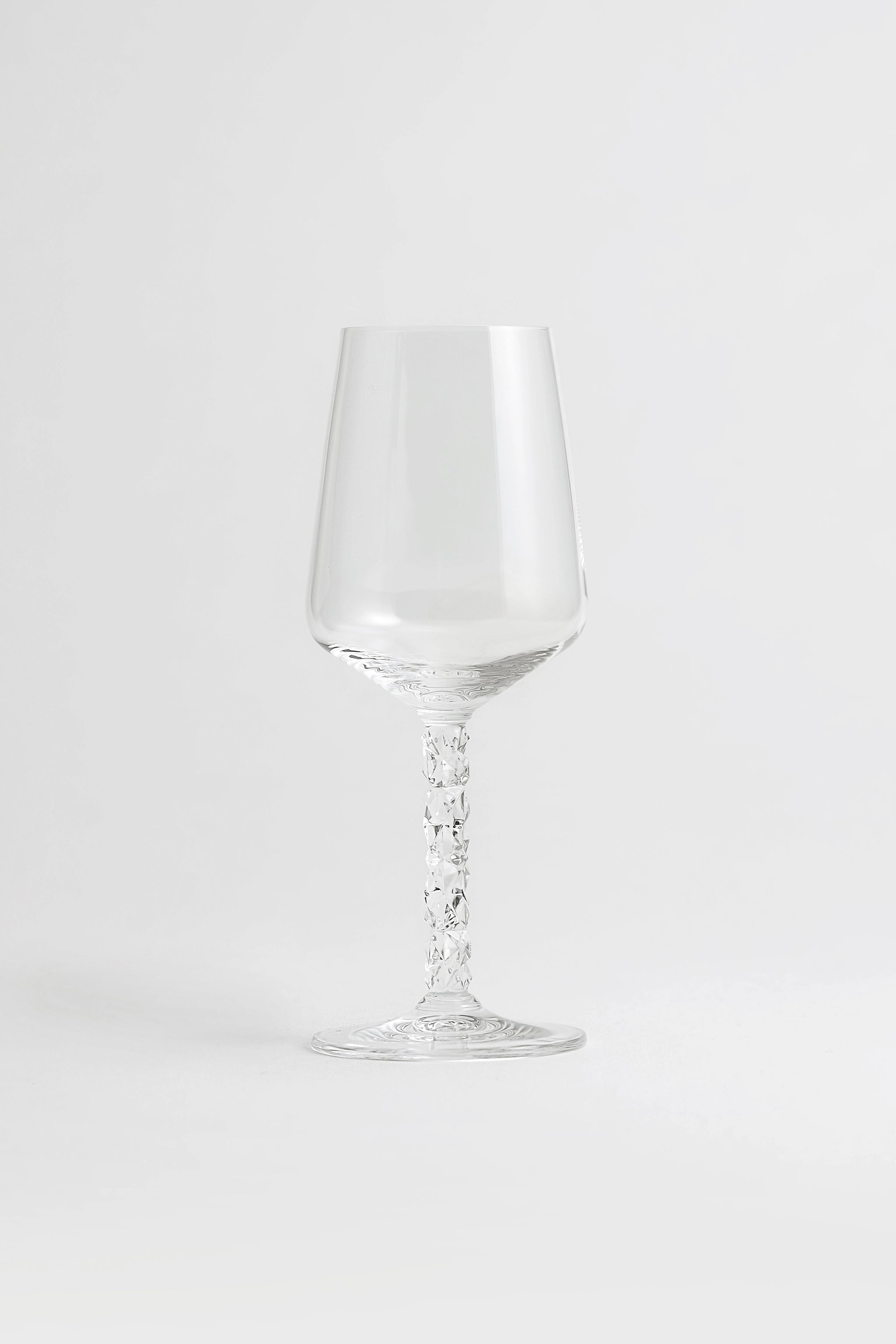 A pair of Orrefors Carat Wine Glasses (14.8oz) with textured stems stand elegantly on a white surface, highlighting their crystal clarity against a plain light background.