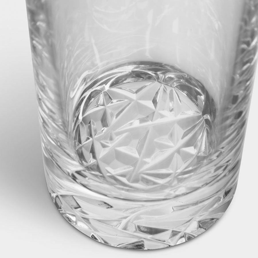 Close-up of an empty, clear crystal glass featuring intricate geometric patterns at the base, reminiscent of the Orrefors Carat Highball Glass from a 4-pack set.