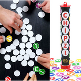 Four hands sort numbered white chips on a black table. Next to them sits a tall, cylindrical Game: Chipzi - Fast Flippin' Fun! container from Tenzi - Carma Games LLC, showcasing vibrant numbers and the word “CHIPZI” displayed vertically—a perfect setup for this fast family game featuring 49 chips numbered 1-7 in seven colors.