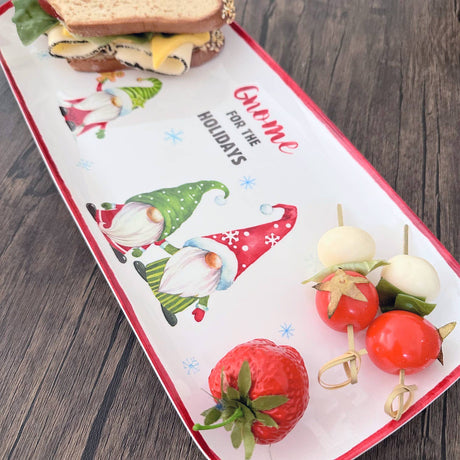 Rectangular melamine tray with Scandinavian holiday gnomes, holding a sandwich, mozzarella and tomato skewers, and a strawberry on a wooden table.