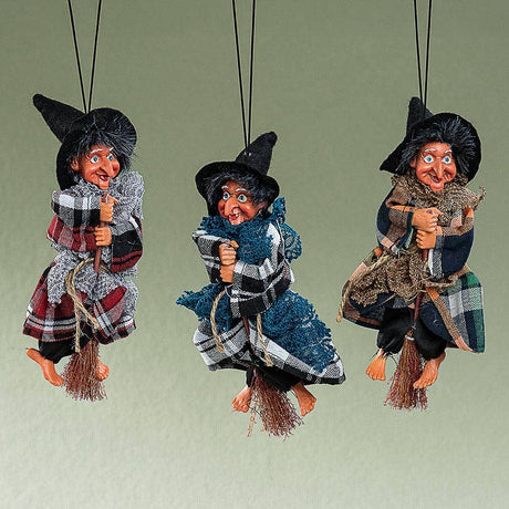The Kitchen Witch: Minna Red Doll, in a plaid robe and black hat, sits on a broom suspended by string—perfect as a folklore-inspired kitchen decor piece and charming good luck doll for your home.