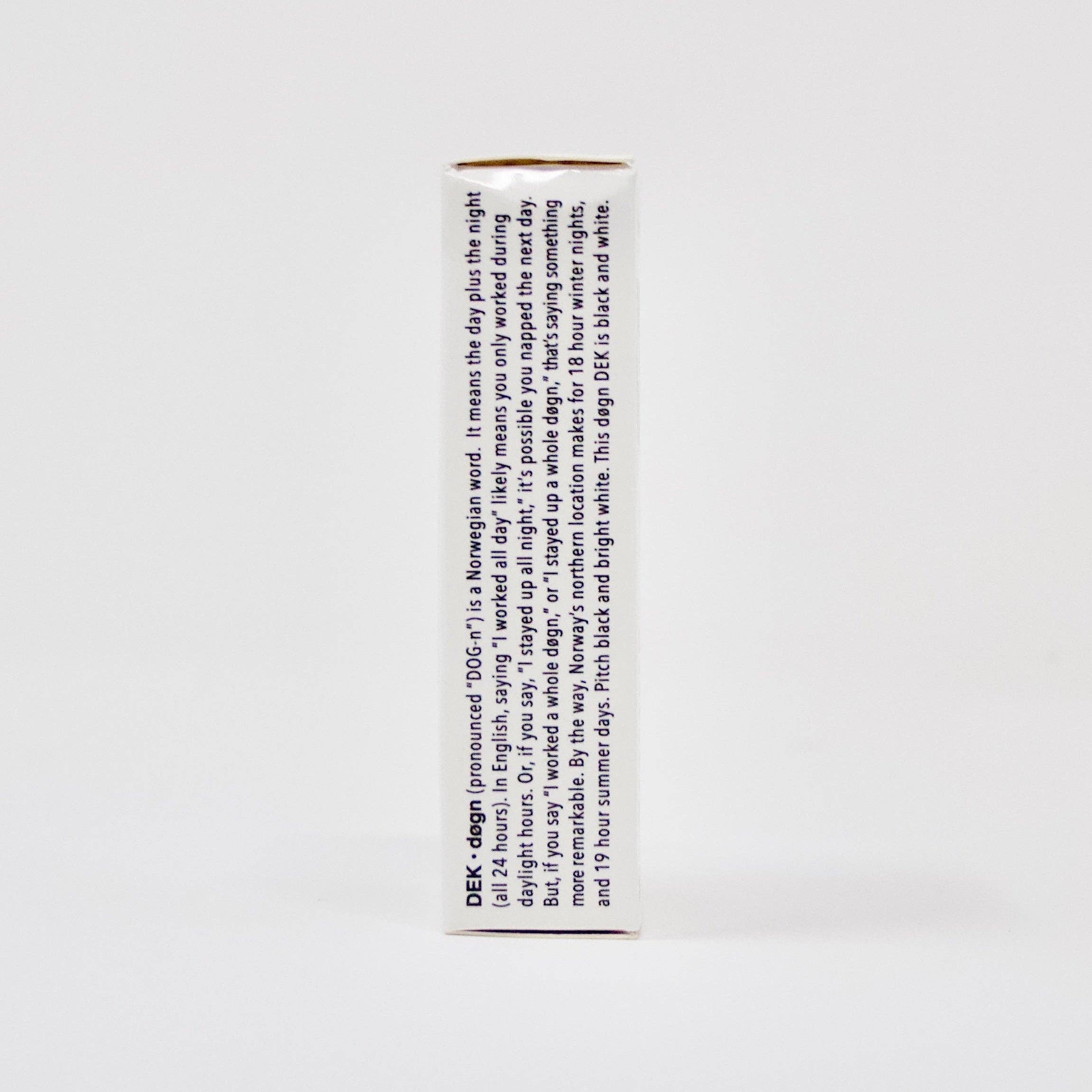 The side view of the DEK Døgn (Norway) playing card box displays text in blue. The predominantly white, rectangular box captures a distinctive aesthetic influenced by Norwegian design.