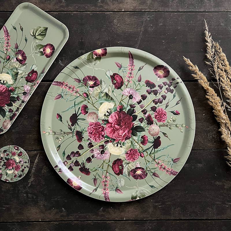 Round Nordic birch veneer tray with red, pink, and white flowers and green leaves on a muted green background, placed on a dark wooden surface.