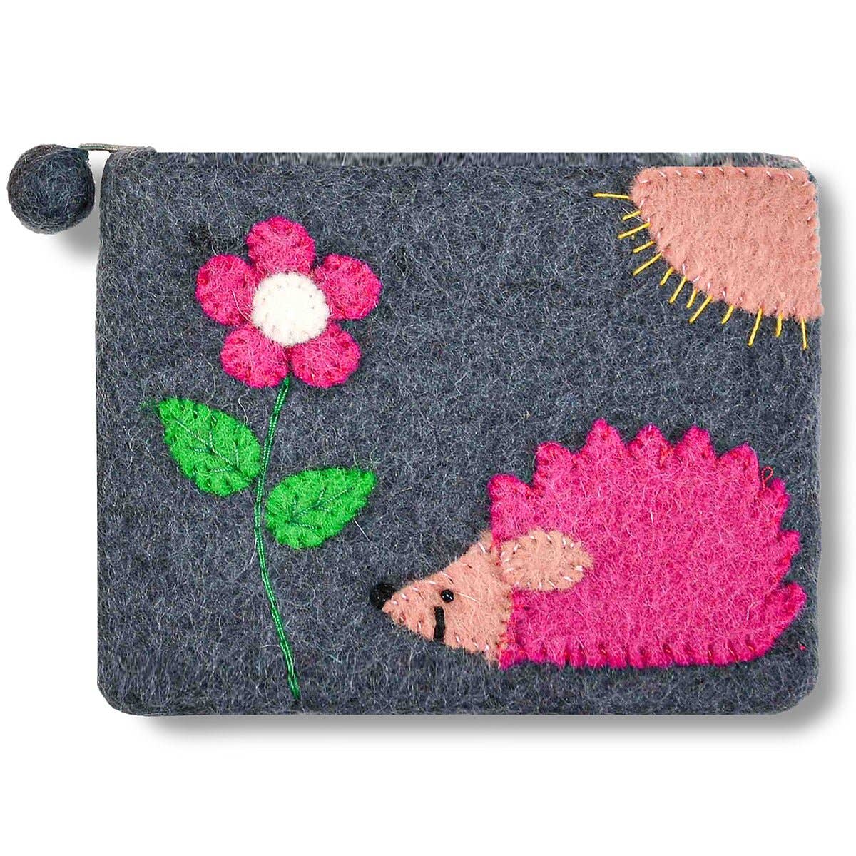 The Grey Hedgehog and Flower Coin Purse is a gray wool felt bag, handcrafted in Nepal, with a pink felt hedgehog, pink flower with green leaves, and a stitched partial pink sun on the front.