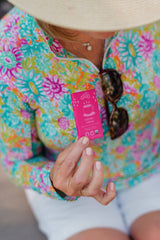 Person wearing a floral shirt and sunhat holds a pink box labeled Coffee + Cream; sunglasses hang from the shirt collar. Box mentions Ethiopian coffee chocolate.