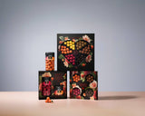 Four boxes and one jar of colorful chocolate-coated licorice from Lakrids by Bülow are arranged on a light surface against a plain background. The Gift Box LOVE 2026 packaging is adorned with decorative floral designs and heart-shaped windows that reveal the assorted chocolates inside, including the 4 Flavor Selection Love Box featuring gluten-free confections inspired by Scandinavian chocolate traditions.