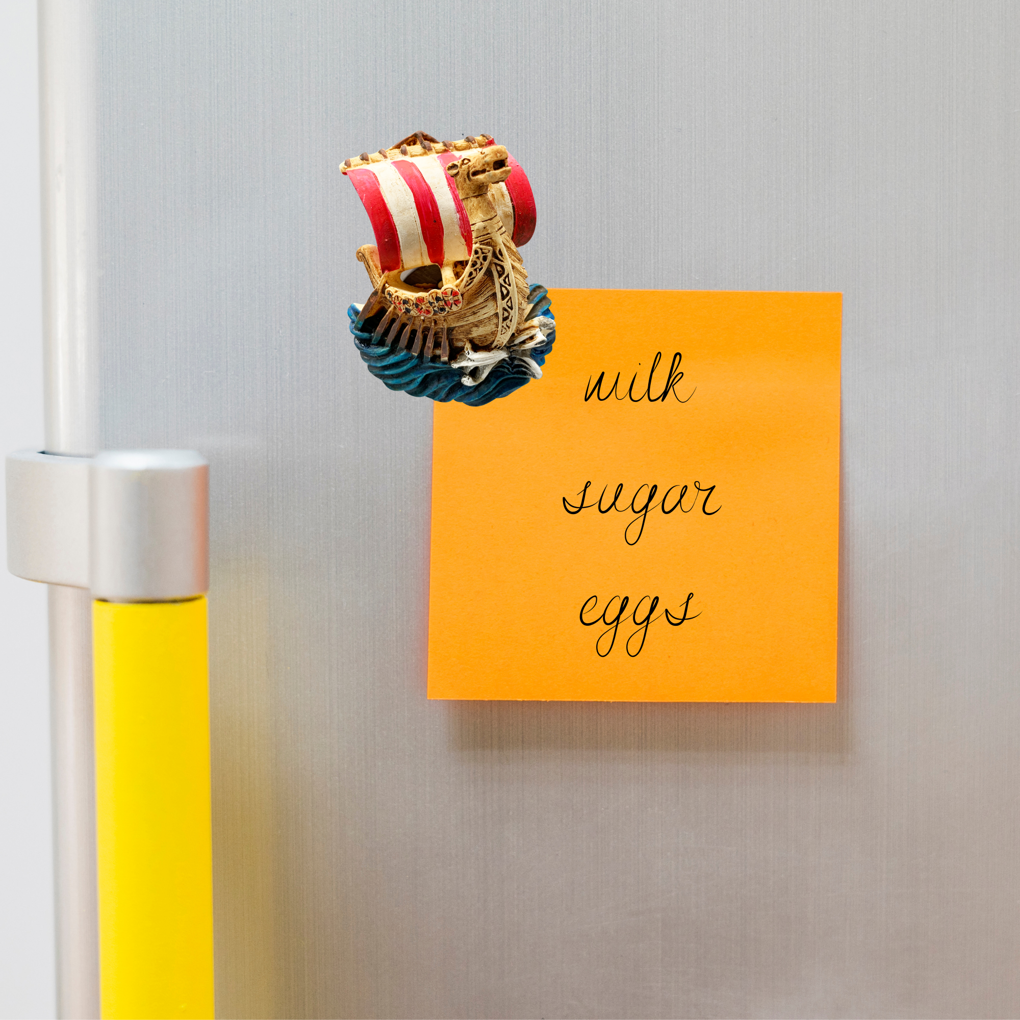 The Magnet: Viking Ship 3-Dimensional Refrigerator Magnet holds an orange sticky note for milk, sugar, and eggs on a silver fridge—adding a charming Nordic novelty touch to your home decor.