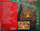 Glowing wooden LED decor with a winter scene placed before a fireplace; packaging displays text descriptions in several languages.