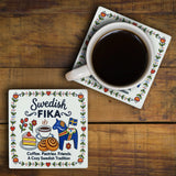 Two ceramic Swedish coasters decorated with colorful Scandinavian-style Dala horse and pastry illustrations, one supporting a white mug of black coffee.