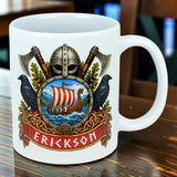 White mug featuring Viking-themed designs with a helmet, crossed axes, two black birds, a longship, and a family name in bold letters on a red banner.