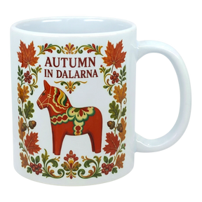 White ceramic mug featuring leaves, flowers, a red Swedish Dala horse, and the text “AUTUMN IN DALARNA” in Scandinavian folk art style.