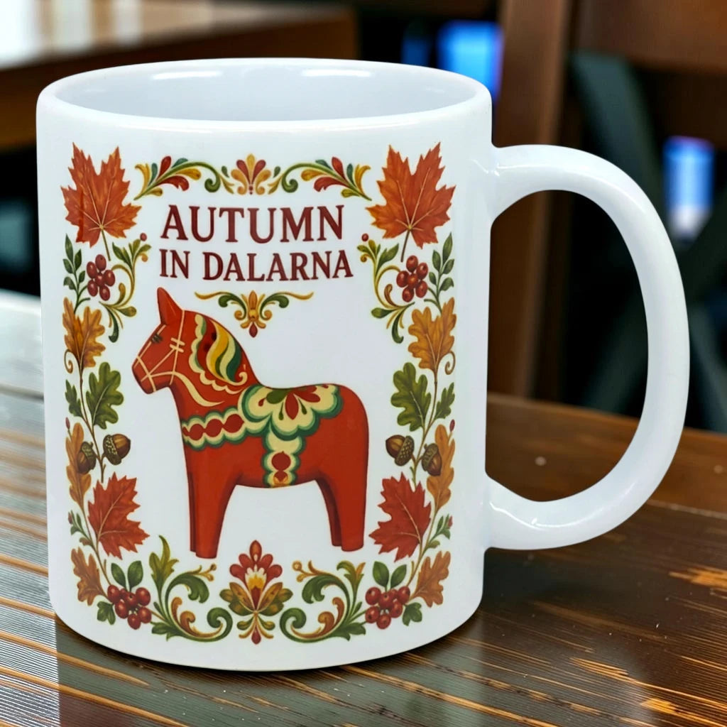 White mug featuring a Swedish Dala horse, autumn leaves, and floral Scandinavian folk art designs, placed on a wooden table.