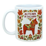 White mug featuring colorful floral patterns, a red Swedish Dala horse, and “AUTUMN IN DALARNA” text encircled by autumn leaves in Scandinavian folk art style.