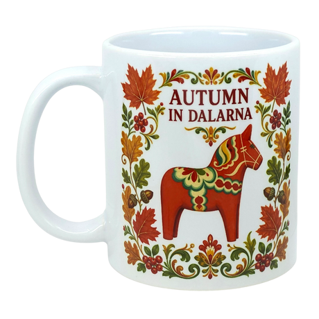White mug featuring colorful floral patterns, a red Swedish Dala horse, and “AUTUMN IN DALARNA” text encircled by autumn leaves in Scandinavian folk art style.