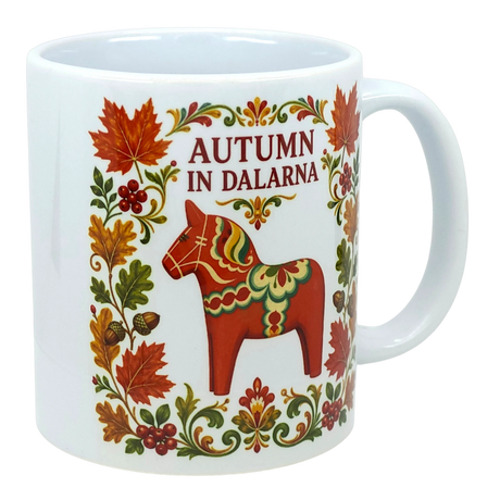 White mug featuring Scandinavian folk art with autumn leaves, acorns, a red Dala horse, floral patterns, and text reading “Autumn in Dalarna.”.