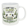 The Nordic Wholesale "Better at Pickleball" Ceramic Gnome Mug (11 oz) features two Nordic gnomes with paddles, net, and ball, green accents, and fun text: "I don't get older, I just get better at pickleball!" A perfect gift for pickleball fans.