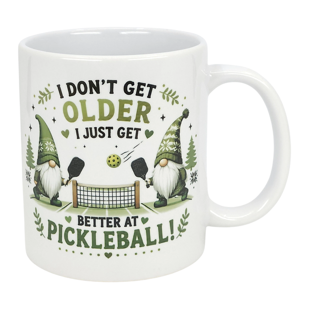 The Nordic Wholesale "Better at Pickleball" Ceramic Gnome Mug (11 oz) features two Nordic gnomes with paddles, net, and ball, green accents, and fun text: "I don't get older, I just get better at pickleball!" A perfect gift for pickleball fans.