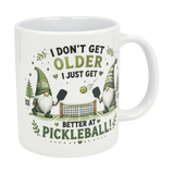 The Nordic Wholesale Mug: Better at Pickleball Ceramic Gnome Mug (11 oz) features two green-hatted Nordic gnomes playing pickleball, a net and ball, and the text: I don't get older, I just get better at pickleball!.