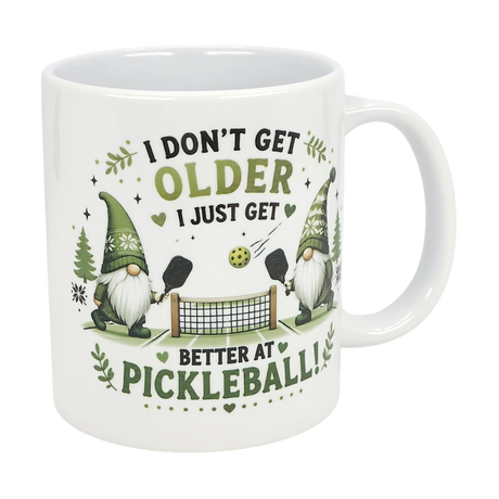 The Nordic Wholesale Mug: Better at Pickleball Ceramic Gnome Mug (11 oz) features two green-hatted Nordic gnomes playing pickleball, a net and ball, and the text: I don't get older, I just get better at pickleball!.