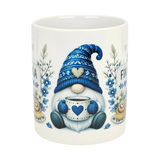 The Nordic Wholesale Mug: Blue Tomte Gnome Fika Ceramic Mug (11 oz) features a Scandinavian gnome with a blue hat, holding a heart mug, surrounded by blue flowers and pastries. "FIKA" appears in the background.