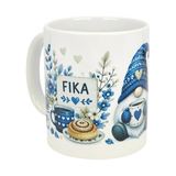 The Nordic Wholesale Mug: Blue Tomte Gnome Fika Ceramic Mug (11 oz) features a Scandinavian gnome in a knit hat with blue floral and heart accents, holding coffee and pastry near a FIKA sign.
