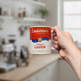 A hand holds the Swedish Gift Store’s 11oz ceramic mug, designed like a soup can label reading “Lindstrom’s Condensed Extra Chunky Cream of Lutefisk Soup,” with a blurred kitchen backdrop—an ideal Scandinavian heritage gift.