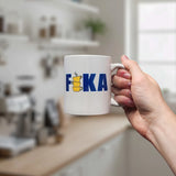 A hand holds the Swedish Gift Store’s Mug: FIKA Stacked Cups Swedish Flag Colors Ceramic Mug (11 oz), with “FIKA” in blue and a yellow cup stack for the “I,” standing out against a blurred kitchen background.
