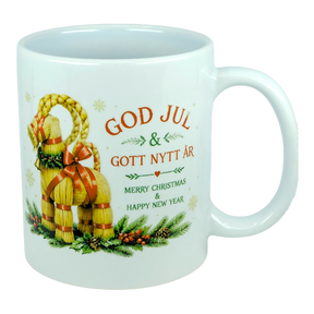 The Nordic Wholesale Mug: God Jul Yule Goat Ceramic Mug (11 oz Capacity) is a white mug decorated with a traditional Swedish Julbock—the straw Scandinavian Yule Goat—embellished with red ribbons and festive greenery. The mug features the greeting "God Jul & Gott Nytt År" in Swedish and its English translation, "Merry Christmas & Happy New Year.