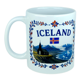 The Mug: Iceland Church Mountain Ceramic Mug (11 oz Capacity) by Nordic Wholesale features a white design adorned with the word "Iceland," the national flag, a scenic Nordic mountain landscape, a black church, and vibrant blue, orange, and red floral patterns around the rim—making it a perfect gift to celebrate Icelandic heritage.