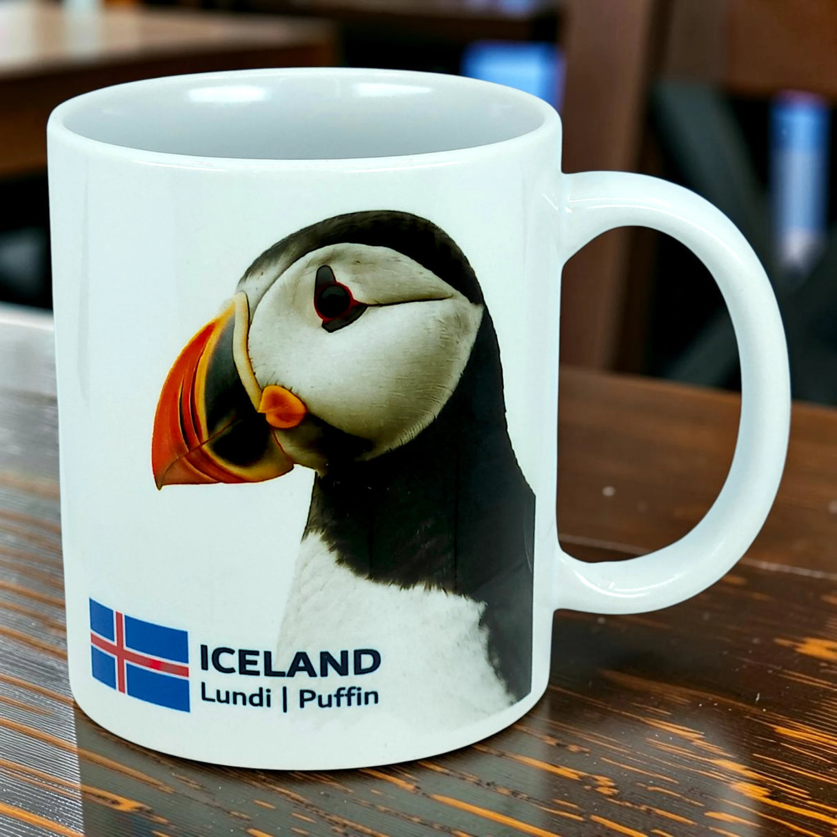 A white ceramic mug by Nordic Wholesale, the "Mug: Iceland National Animal Puffin Ceramic Coffee Mug (11 oz Capacity)," features a charming puffin illustration, the Icelandic flag, and the words "ICELAND Lundi | Puffin." Perfect for Nordic wildlife lovers or anyone who wants to celebrate Iceland's iconic national animal with every sip.