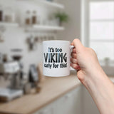 A hand holds the Swedish Gift Store's 11 oz white ceramic mug, "It's Too Viking Early For This," in a bright modern kitchen with blurred shelves and a window in the background.