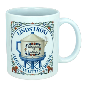 Introducing the Nordic Wholesale Mug: Lindstrom America's Little Sweden Ceramic Coffee Mug (11 oz)—featuring a charming decorative design with a water tower labeled "Välkommen till Lindström," surrounded by floral motifs inspired by Scandinavian folk art and the phrase "Lindstrom, America’s Little Sweden." A perfect mug for celebrating your Swedish heritage.