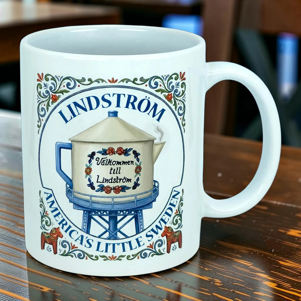 White mug with blue text reading “Lindström, Americas Little Sweden,” an illustrated water tower, and Swedish-style floral designs.