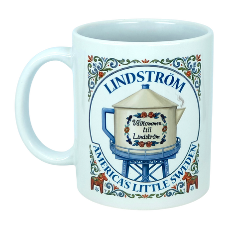 Show your Lindström pride with the Mug: Lindstrom America's Little Sweden Ceramic Coffee Mug (11 oz) by Nordic Wholesale. This white ceramic mug features a decorative illustration of a water tower labeled "Lindström," adorned with Swedish-style floral accents inspired by Scandinavian folk art, along with the phrases "Välkommen till Lindström" and "America’s Little Sweden." A charming keepsake or gift for anyone celebrating their Lindström roots and Swedish heritage.