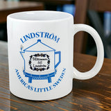 The Swedish Gift Store’s 11 oz ceramic mug features a blue teapot design inspired by the Lindstrom Coffee Pot Water Tower, with "America's Little Sweden" and “Välkommen till Lindström” displayed on its white surface.