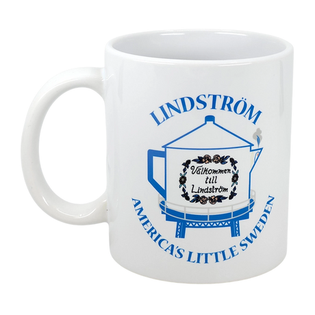 The Nordic Wholesale 11 oz ceramic mug features a blue graphic of the Lindström Coffee Pot Water Tower, Välkommen till Lindström sign with flowers, and "LINDSTRÖM AMERICA'S LITTLE SWEDEN" text.