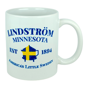 This 11 oz white ceramic mug from Nordic Wholesale features blue text that reads "Lindstrom Minnesota EST 1894 America’s Little Sweden," along with a yellow and blue Swedish flag shaped like the state of Minnesota. The perfect mug for anyone proud of their Lindstrom roots and Swedish heritage. Product name: Mug: Lindstrom Minnesota America's Little Sweden Ceramic Mug (11 oz Capacity).