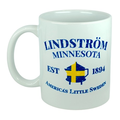 Celebrate Lindstrom’s rich heritage with the Nordic Wholesale Mug: Lindstrom Minnesota America's Little Sweden Ceramic Mug (11 oz Capacity), featuring blue text—“Lindström Minnesota EST 1894 America’s Little Sweden”—and an illustration of a Swedish flag over a coffee pot, perfect for anyone proud of their Swedish roots.