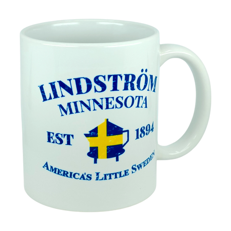 Show off your heritage with the Nordic Wholesale Mug: Lindstrom Minnesota America's Little Sweden Ceramic Mug (11 oz Capacity), featuring blue text, a yellow and blue Swedish flag in the center, and a classic white ceramic finish—ideal for anyone looking for a unique Swedish heritage mug.