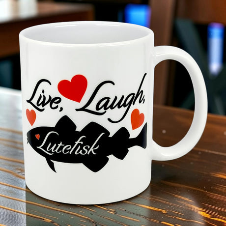 The Nordic Wholesale "Live, Laugh, Lutefisk" 11oz ceramic mug features red hearts and a fish silhouette—ideal as a lutefisk gift or for fans of Scandinavian humor.