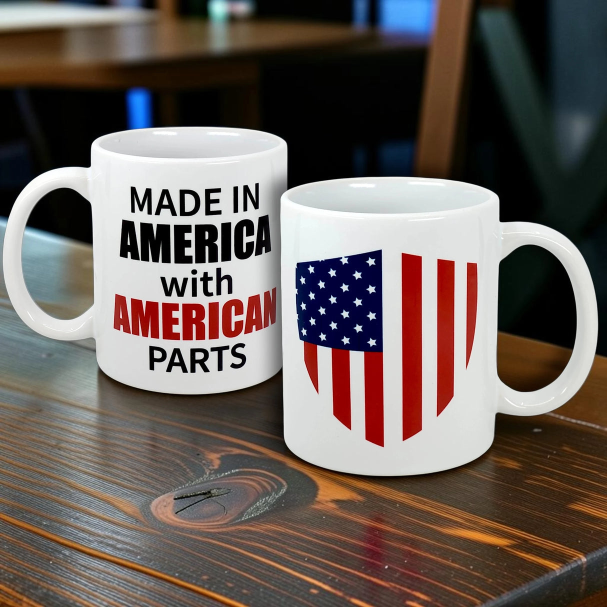 Two white mugs rest on a wooden table: one features an American flag shield, while the other is the Swedish Gift Store's "Mug: Made in America with American Parts Ceramic Mug (11 oz)" with bold black and red text.