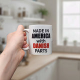 A hand holds the Swedish Gift Store Mug: Made in America with Danish Parts Ceramic Mug (11 oz), featuring bold text—an ideal heritage coffee cup for any bright, modern kitchen.