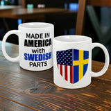 Two white Swedish Gift Store ceramic mugs (11 oz) sit on a wooden table: one says "Made in America with Swedish Parts" in black and blue, the other features a shield blending the American and Swedish flags.