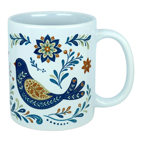 The Nordic Wholesale Mug: Nordic Folk Art Birds Ceramic Mug (11 oz Capacity) is a white Scandinavian-style ceramic mug showcasing a decorative blue bird encircled by detailed floral motifs in blue, orange, and gold hues. It features a plain background and a large handle.