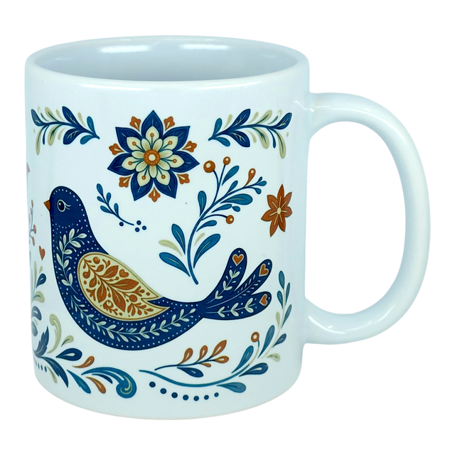 The Nordic Wholesale Mug: Nordic Folk Art Birds Ceramic Mug (11 oz Capacity) is a white Scandinavian-style ceramic mug showcasing a decorative blue bird encircled by detailed floral motifs in blue, orange, and gold hues. It features a plain background and a large handle.